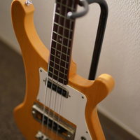 ギタースタンドに立てかけたナチュラル木目のエレキベースの写真