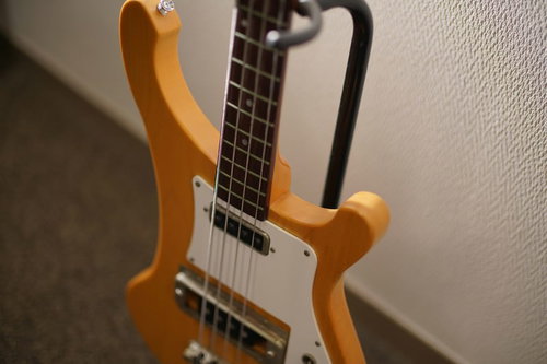 ギタースタンドに立てかけたナチュラル木目のエレキベース