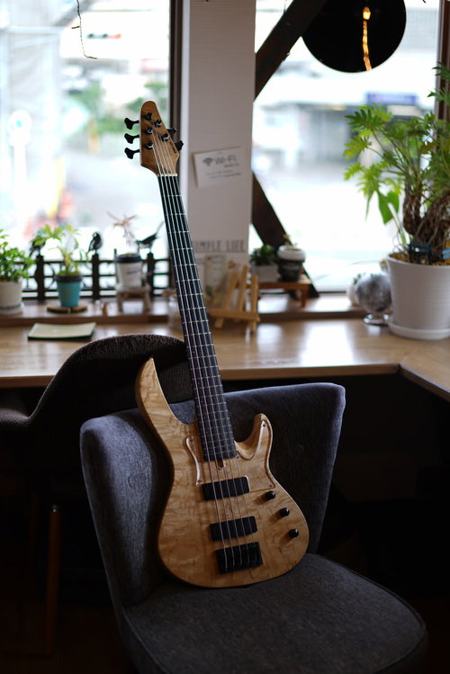カフェの椅子に立てかけた5弦ベース、自然光で映える木目のナチュラルカラー