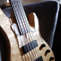 ナチュラルな木目の5弦ベース、ペグとボディの細部が鮮明に写された楽器の写真