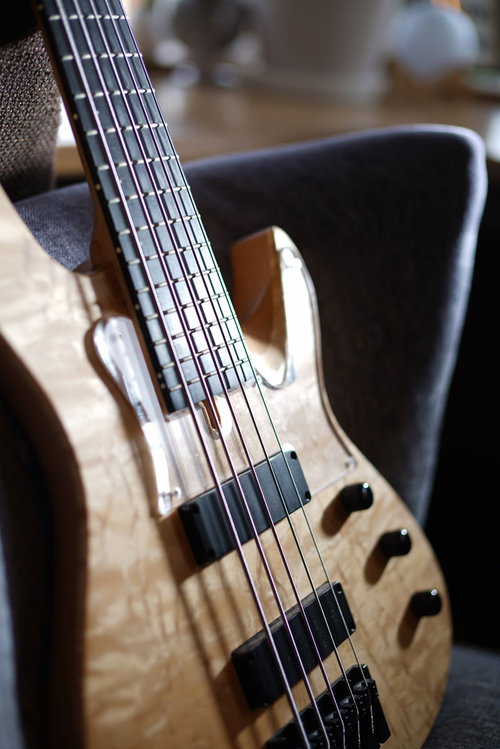 ナチュラルな木目の5弦ベース、ペグとボディの細部が鮮明に写された楽器