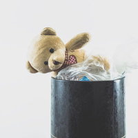 赤いチェック柄リボンの茶色いぬいぐるみが入った金属のゴミ箱の写真