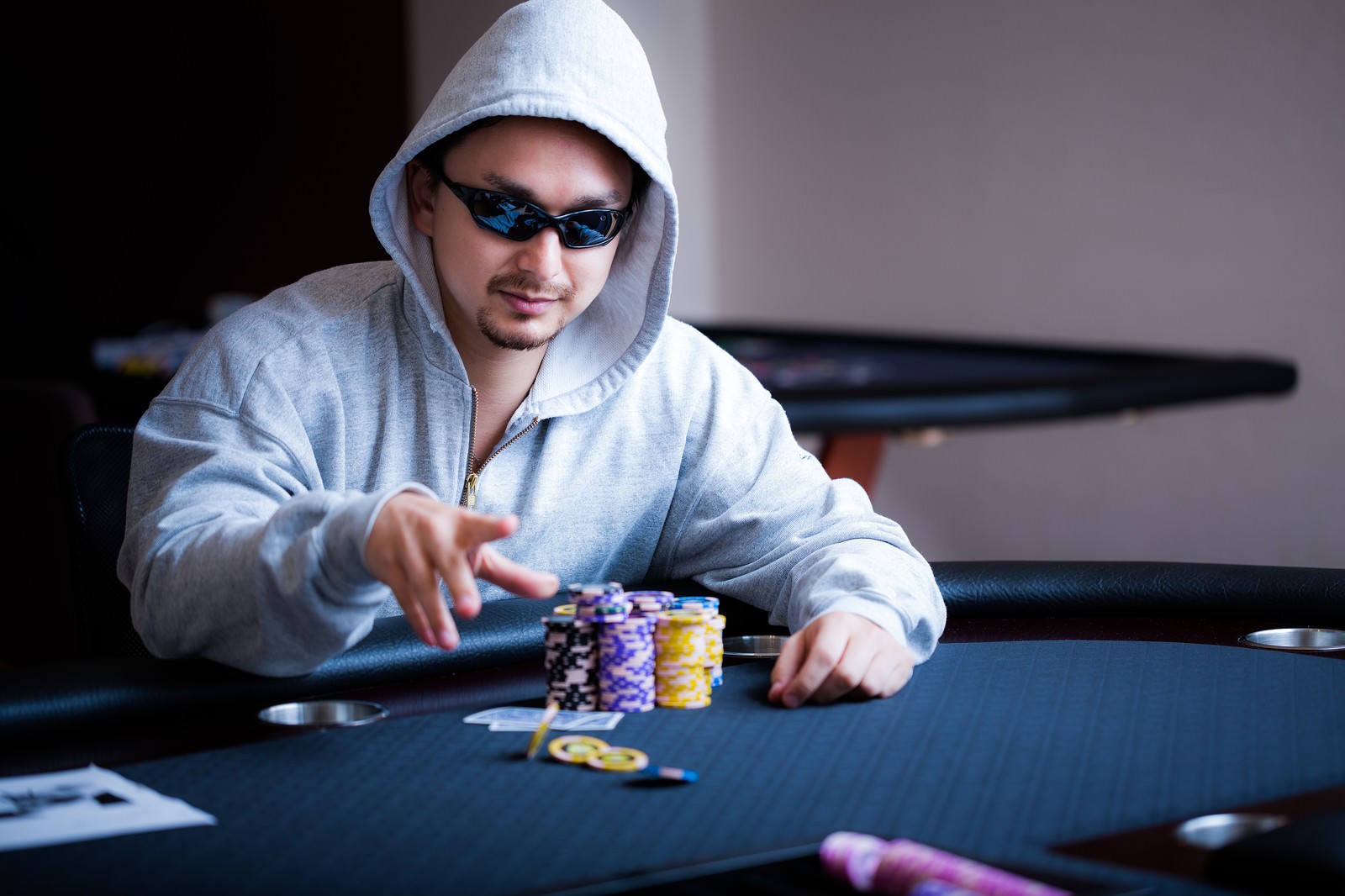 ポーカーテーブルでサングラスをかけた男性がポーカーチップに手を伸ばしている［モデル：Max_Ezaki］