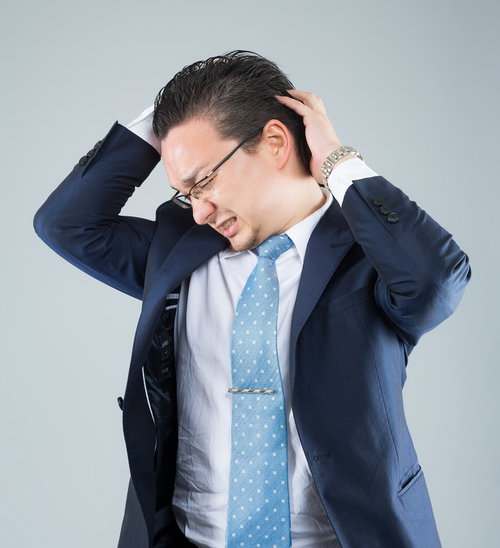 頭を抱えて悩むビジネスマン、眼鏡とネクタイ姿で困惑する男性