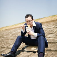 土手で昼食を済ます営業中のビジネスマンの写真
