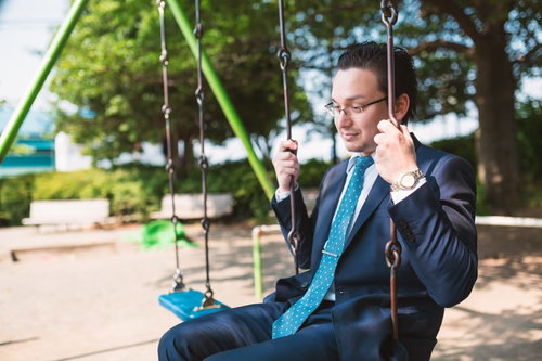 ノスタルジックな表情の外資系サラリーマンがブランコに座る