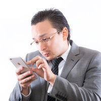 スマホ画面をピンチインして見る灰色スーツの眼鏡の男性の写真