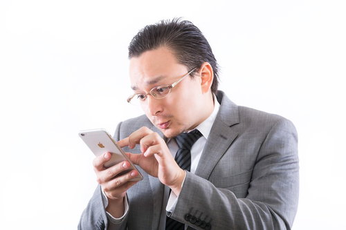 スマホ画面をピンチインして見る灰色スーツの眼鏡の男性