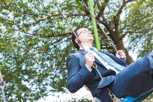公園のブランコに座って顔を上げるスーツの眼鏡の男性