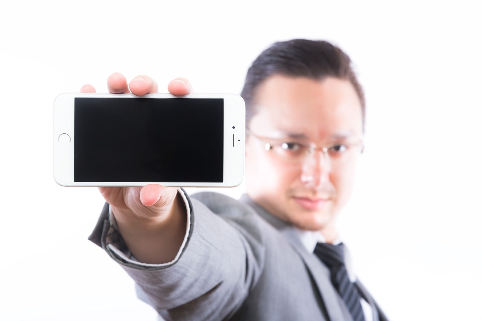 スマートフォンの画面を正面にかざすスーツ姿の男性［モデル：Max_Ezaki］