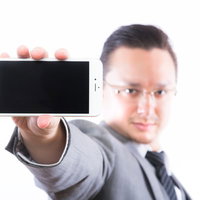 スマートフォンの画面（横）を見せるエンジニアの写真