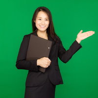 資料を持ってグリーンバックで案内する黒スーツの女性の写真