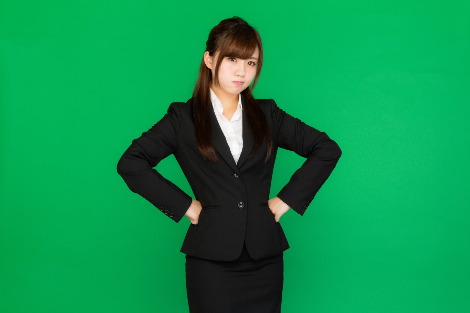 グリーンバックで両手を腰に当てて怒るビジネス女性［モデル：河村友歌］