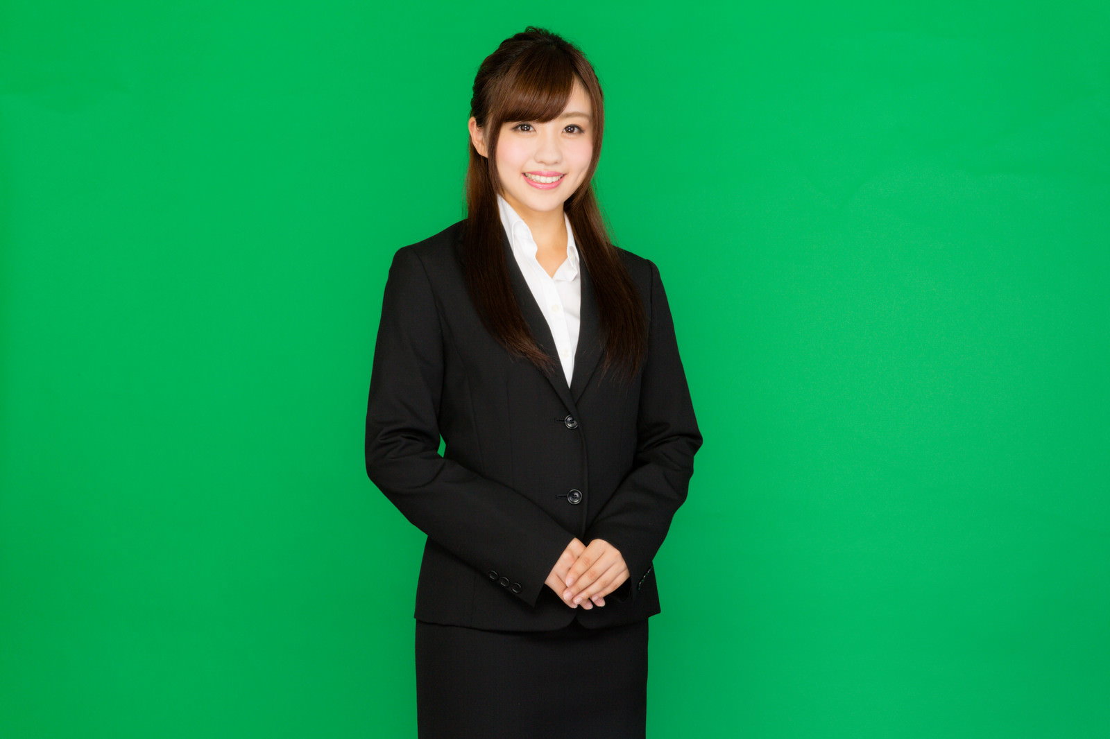 グリーンバックの前で手を重ねて微笑む就活スーツの女性［モデル：河村友歌］