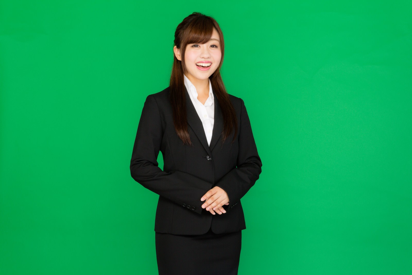 グリーンバックの前で小馬鹿にした笑いを浮かべるスーツ姿の女性［モデル：河村友歌］