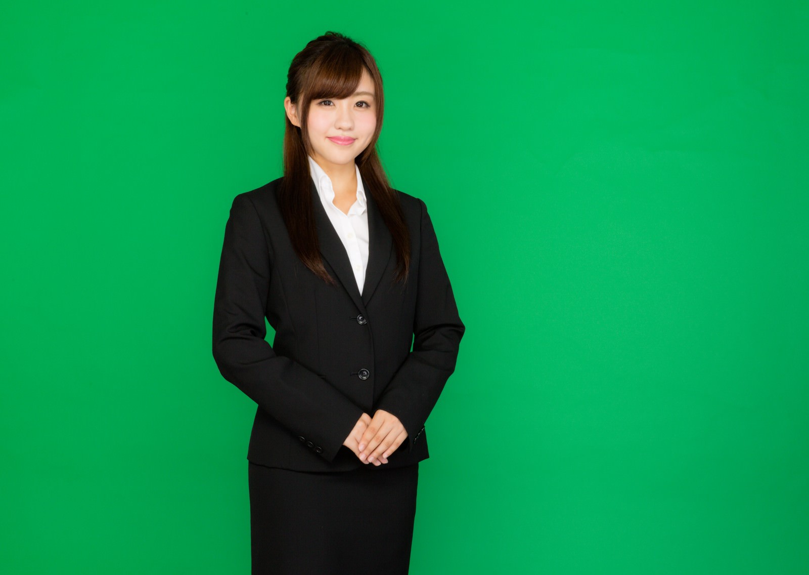 グリーンバック前で微笑む黒スーツの女性受付嬢［モデル：河村友歌］
