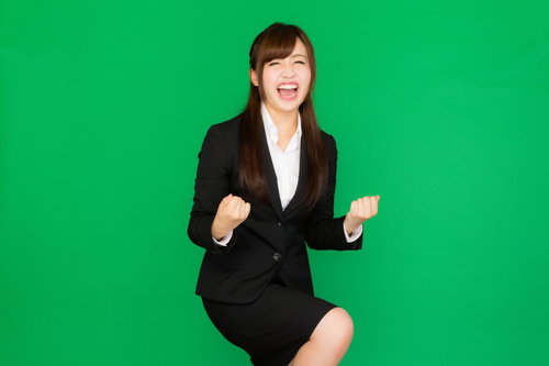 社内プレゼンが通って喜ぶスーツ姿の女性、ガッツポーズ（グリーンバック）
