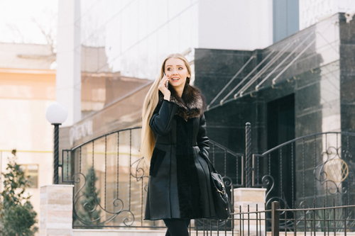 黒いコートを着て電話しながら屋外を歩くモデル