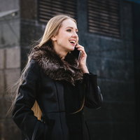 黒いコートで屋外でスマホ通話する笑顔の外国人女性の写真