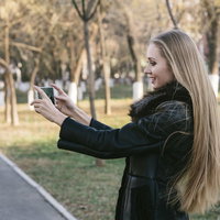 公園で両手に持ったスマホで撮影するモデルの写真