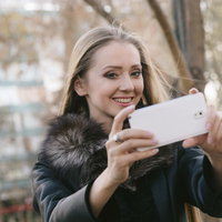 スマホを使って屋外で撮影中のブロンド女性の写真