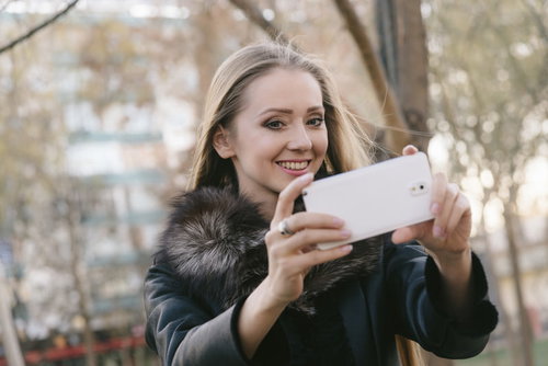 スマホを使って屋外で撮影中のブロンド女性