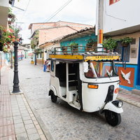 南米のカラフルな街並みを走る白いトゥクトゥクの写真