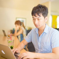 木製テーブルでノートPCと南国ドリンクを前に作業する男性の写真
