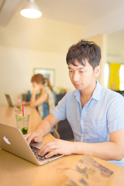 木製テーブルでノートPCと南国ドリンクを前に作業する男性