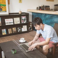 茶色い椅子に座りノートPCとコーヒーでカフェ作業する男性の写真