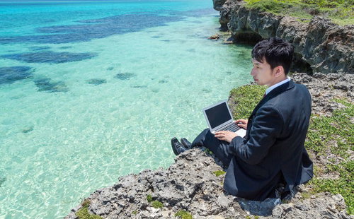 岩場に座ってノートPCを操作するスーツのビジネスマン