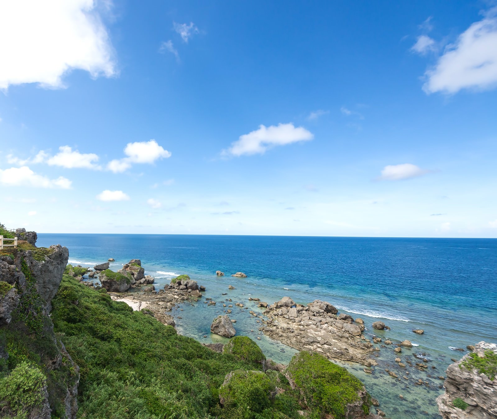 緑の植物が生える崖と岩が点在する東平安名崎の海