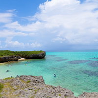 白い砂浜と岩場の浅瀬で泳ぐ人たちのシュノーケリングスポットの写真