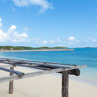 青い海と遠くの島が見える遠浅の砂浜と木の日除け骨組みの写真