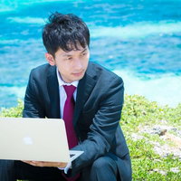 青い海をバックにMacで作業を行うビジネスマンの写真