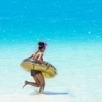 黄色い浮き輪を持って透明な海を走る水着の女性の写真