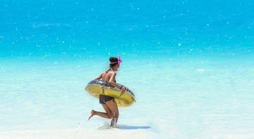 黄色い浮き輪を持って透明な海を走る水着の女性