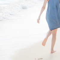 波打ち際の砂浜を手をつないで歩くカップルの後ろ姿の写真