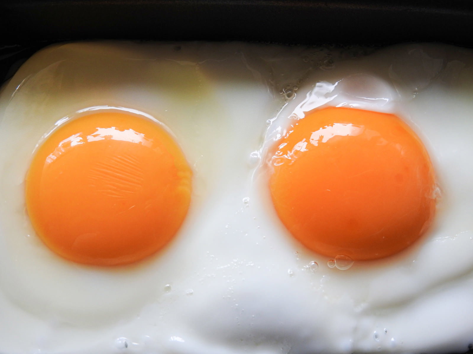 フライパンで焼かれた2つの目玉焼き、オレンジ色の黄身と白い白身