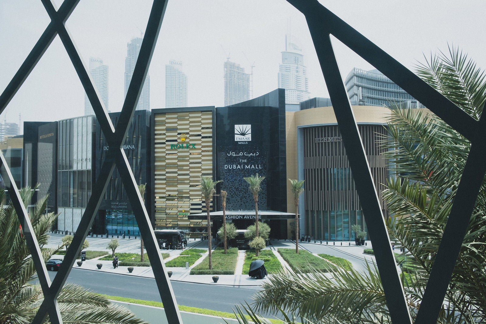 A photograph of the exterior of the Dubai Mall, showcasing its distinctive black frame structure and surrounding landscaping.