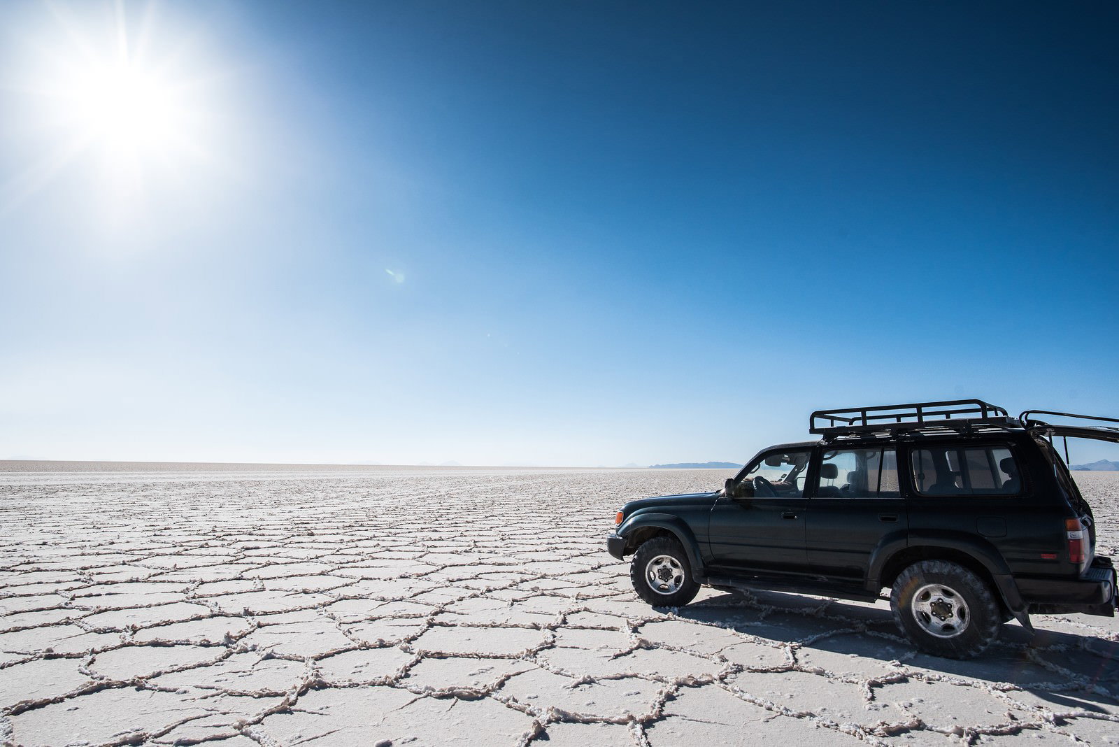 ウユニ塩湖の乾季に停車する黒い4WD。広大な白い塩の大地と青空
