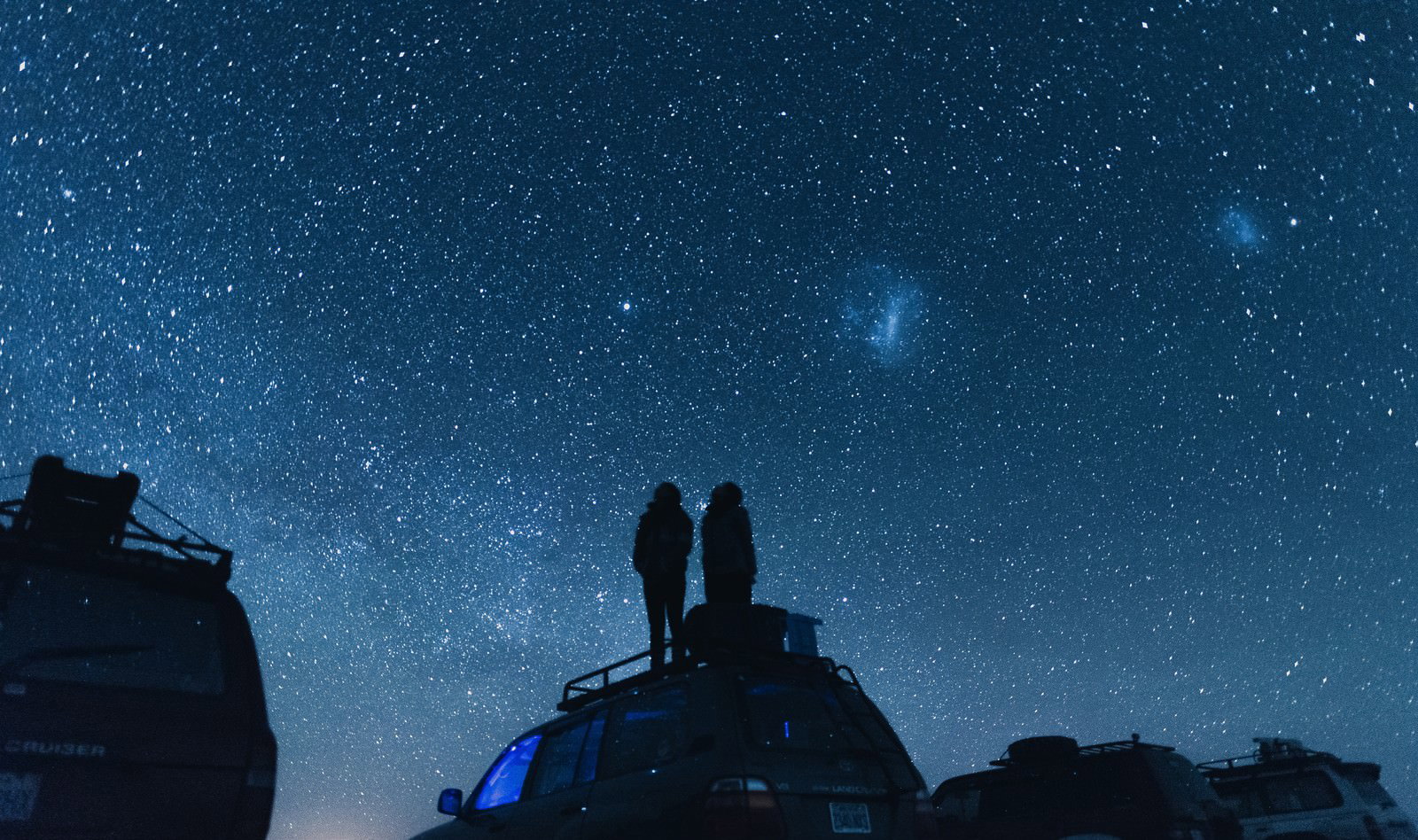 ウユニ塩湖で車の屋根に立つ人物たちが満点の星空を眺めている写真