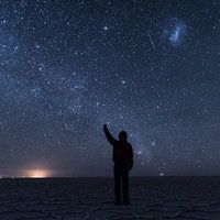 ウユニ塩湖の星空の下で片腕を上げる観光客の写真