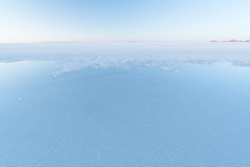 ウユニ塩湖の雨季に映る空と島影、鏡のような水面風景の写真