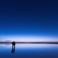 日の出直前のウユニ塩湖で星空を眺めるカップルの写真