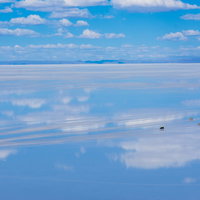 雨季のウユニ塩湖で天空の鏡を横断する車と観光客の写真