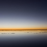 ウユニ塩湖の日没時の地平線に映る夕焼けの風景の写真