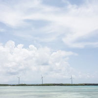 透き通る沖縄の海と風力発電機が立ち並ぶ快晴の空の写真