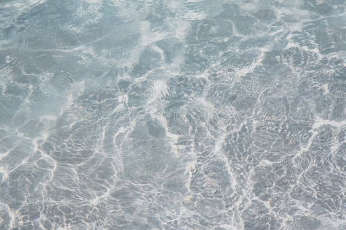 透き通る海の水面に広がる波模様と砂地の浅瀬風景