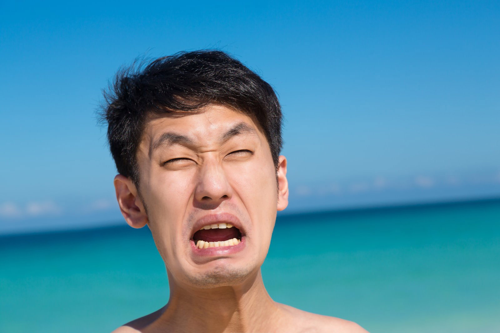 海辺で目を閉じて口を大きく開ける男性のアップ［モデル：大川竜弥］